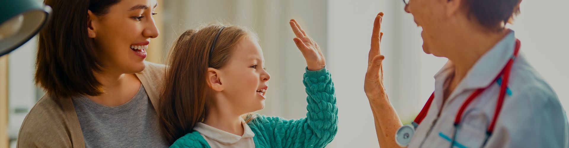 Mama z dziewczynką przybijają piątkę lekarce podczas kontrolnej wizyty lekarskiej w przychodni.